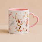 A white ceramic mug with a pink interior and a heart-shaped handle, decorated with vintage-style illustrations including envelopes, wax seals, flowers, and a quote on a warm beige background.