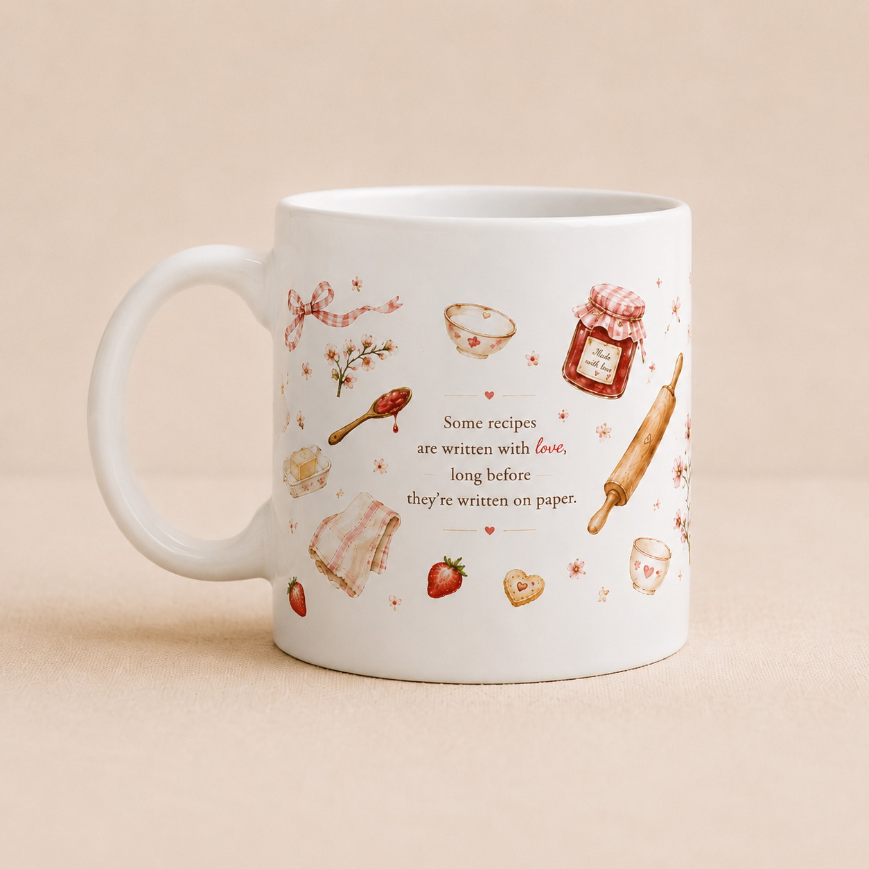 A white ceramic mug with a handle, decorated with delicate watercolor illustrations of baking ingredients and text that reads, 'Some recipes are written with love, long before they're written on paper.' The mug is set against a solid, warm beige background.