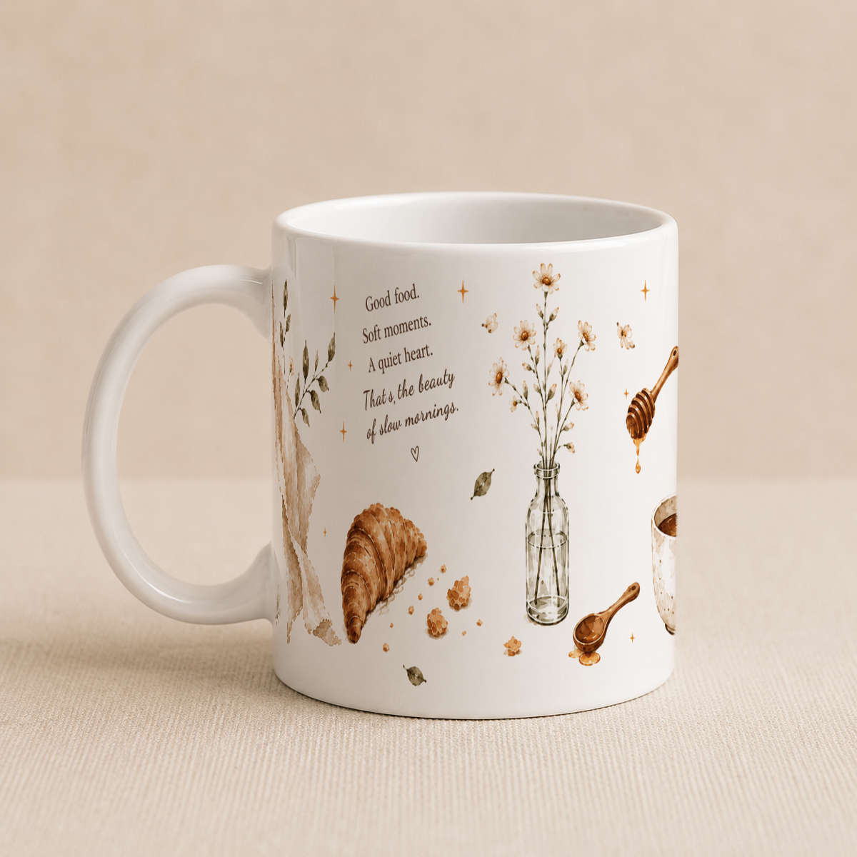 A white ceramic mug with a warm beige background, decorated with illustrations of a croissant, flowers in a vase, a honey dipper, a spoon, and a small quote about good food and soft moments.